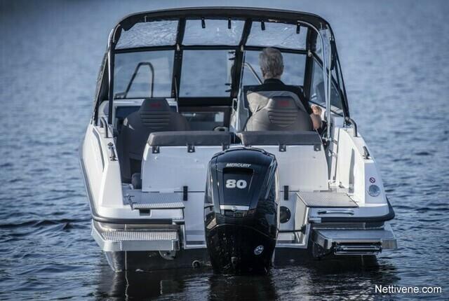 A man sits at the helm of a white boat with a Mercury 80 outboard motor, navigating calm waters.